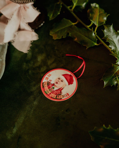 Circular Christmas ornament with Derry Girls Clare character design on green foliage.